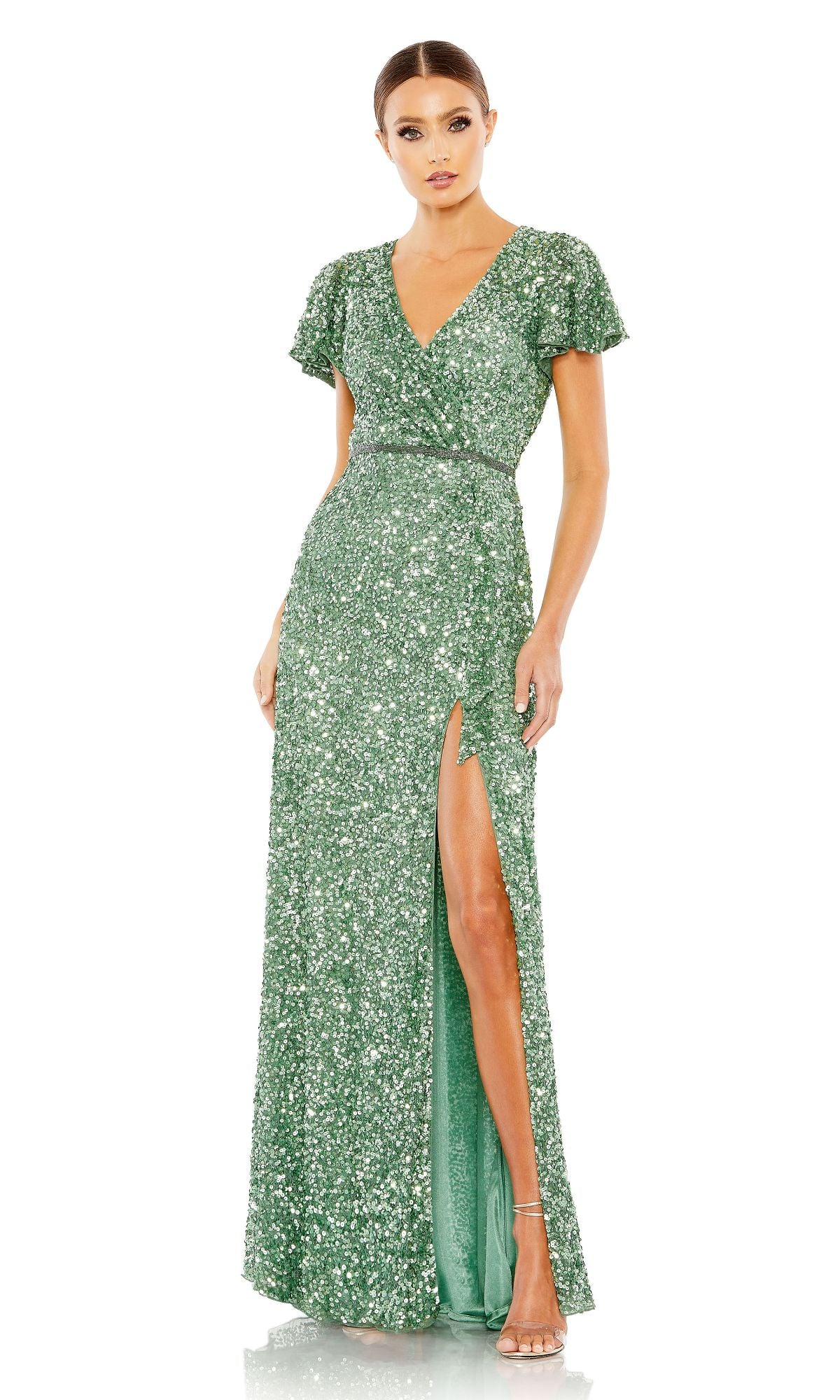 A woman wearing the Mac Duggal 5540 Short-Sleeve Sequin Formal Dress in green, featuring a V-neckline and thigh-high slit, paired with strappy heels.